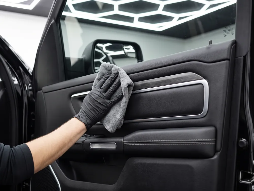 Behandschuhte Hand wischt die Ledertürverkleidung mit einem Mikrofasertuch